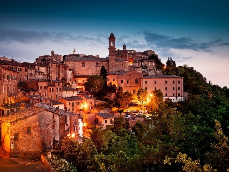 Italian hill village well bell tower and old stone buildings lit up at night