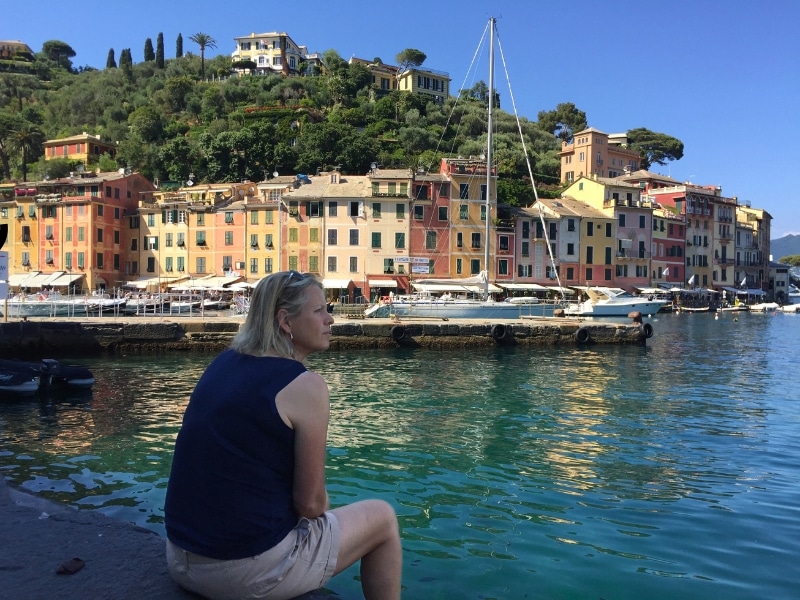 woman sitting on a harbour with boats and colourful houses in the background