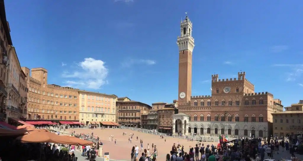 red brick square lined with historic buildings in orange hues and a tall red and cream campanile