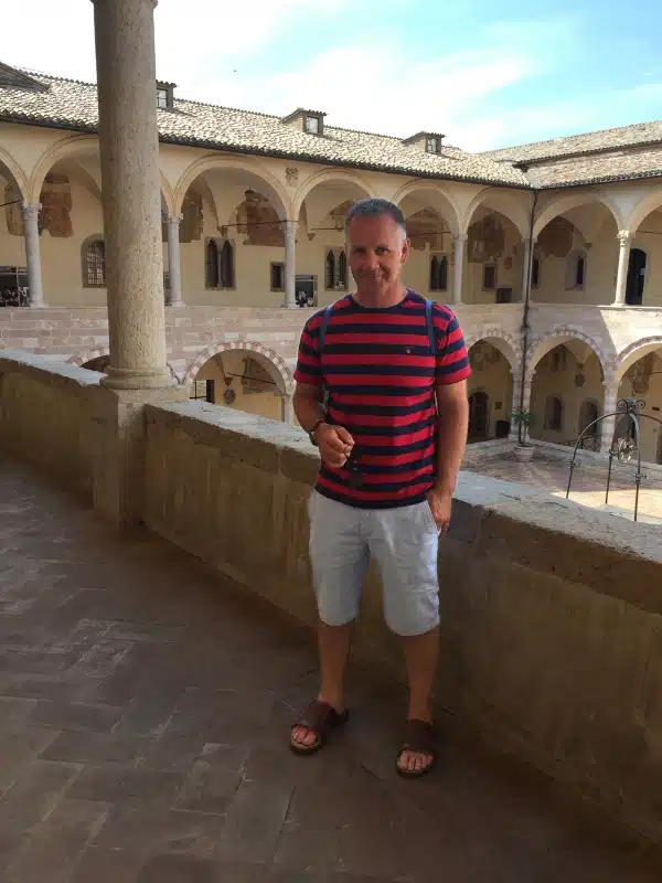 man standing on a first floor cloister made of creamy stone with pillars. and arches