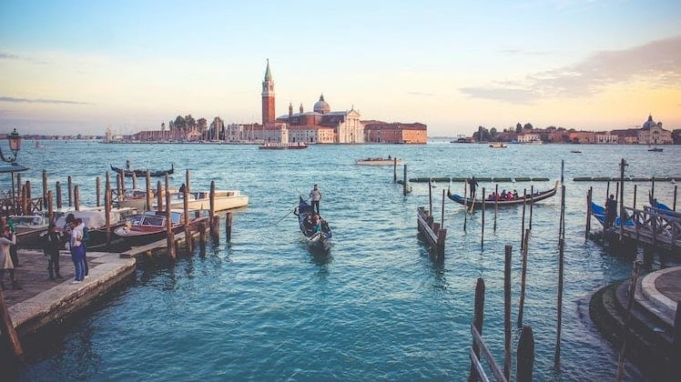 an elegant red brick church in the background, looking over blue waters and and gondolas