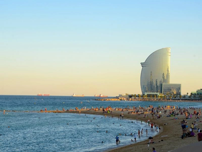 Large sandy beach busy with people and a glass oval hotel at one end