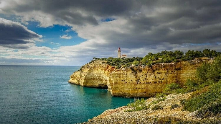 Sandstone cliffs topped with greenery and the lighthouse at Cape St Vincent in the Algarve Portugal