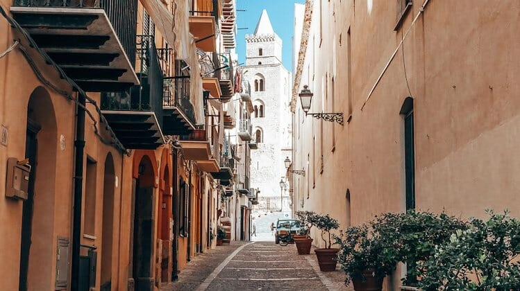 Stone tower glimpsed at the end of a narrow cobbled street in Sicily