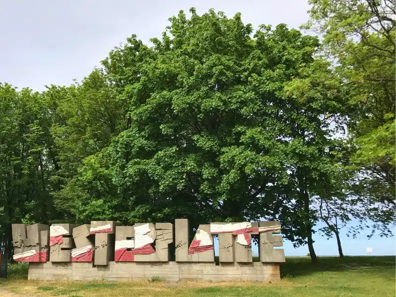 concrete sign "Westerplatte" in front of trees with water in the distance