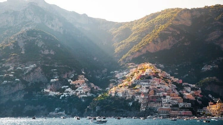 A long view of Positano Italy with colourful houses on the green mountain side and sea with boats in the foreground