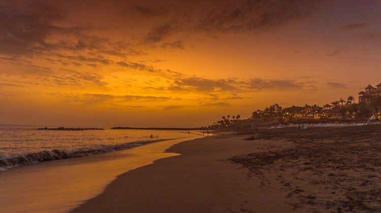 An orange sky above a long beach with houses behind at sunset