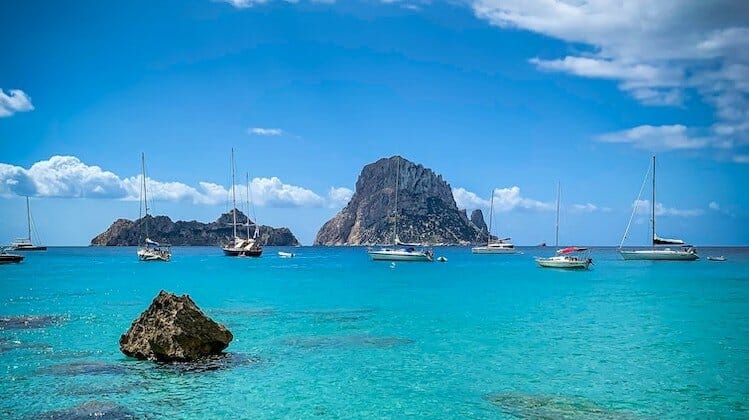 Green sea and blue sky with white yachts on the water and large rocks scattered around