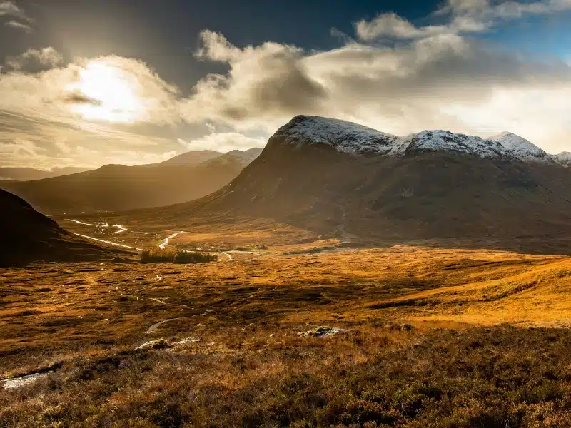 heather and machir line a wide valley in Scotland sheltered by snow capped mountains
