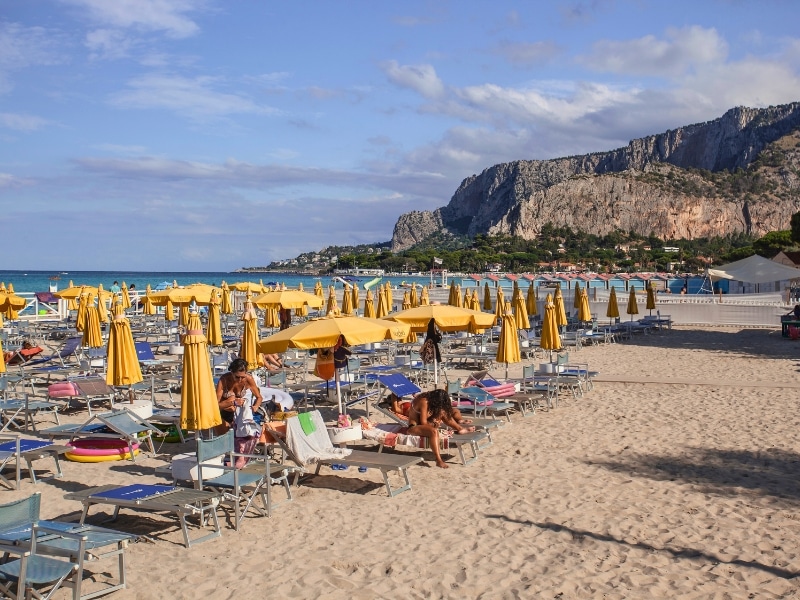 Sandy beach lined with beach beds and ywlloww umberellas