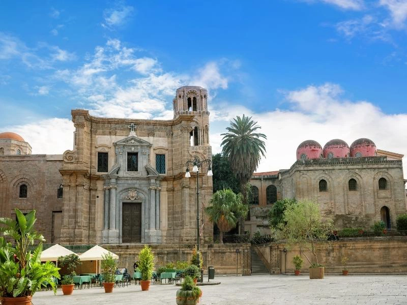 Moorish buildings with domes and towers on a square where there are dining tables and chairs with parasols