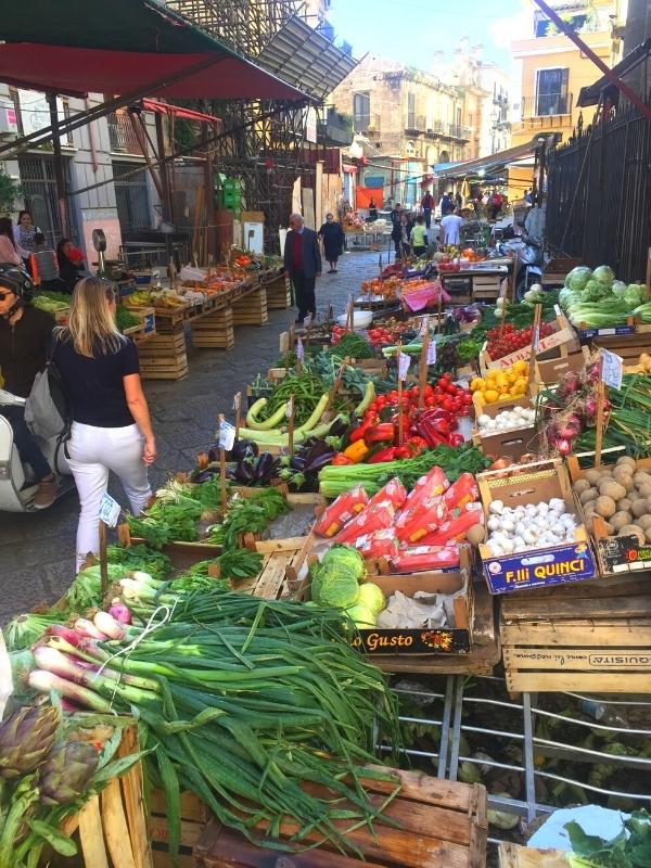 People walking through a street market with stalls of fruit and vegetables lining the road