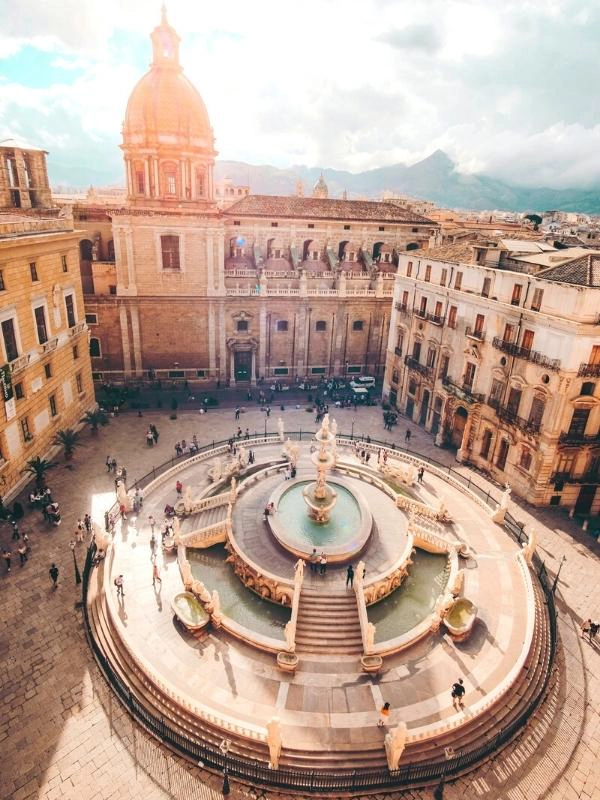 Famous creamy stone fountain surrouned by statues set in a square lined with historic buildings in Italy