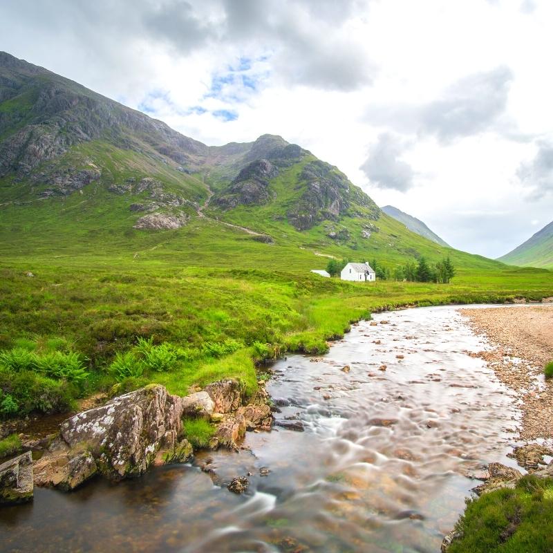 small stream in green valley with small white cottage