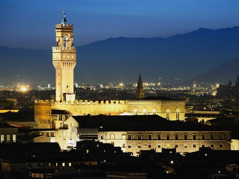 Creamy coloured palace building with crenellated roof and tower, lit up at night