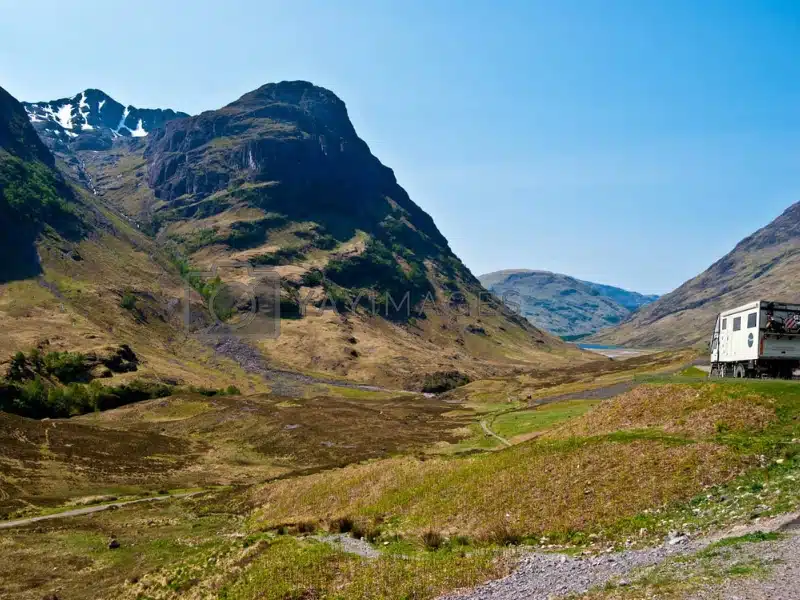 Mountainous valley with a white truck parked on a grassy verge