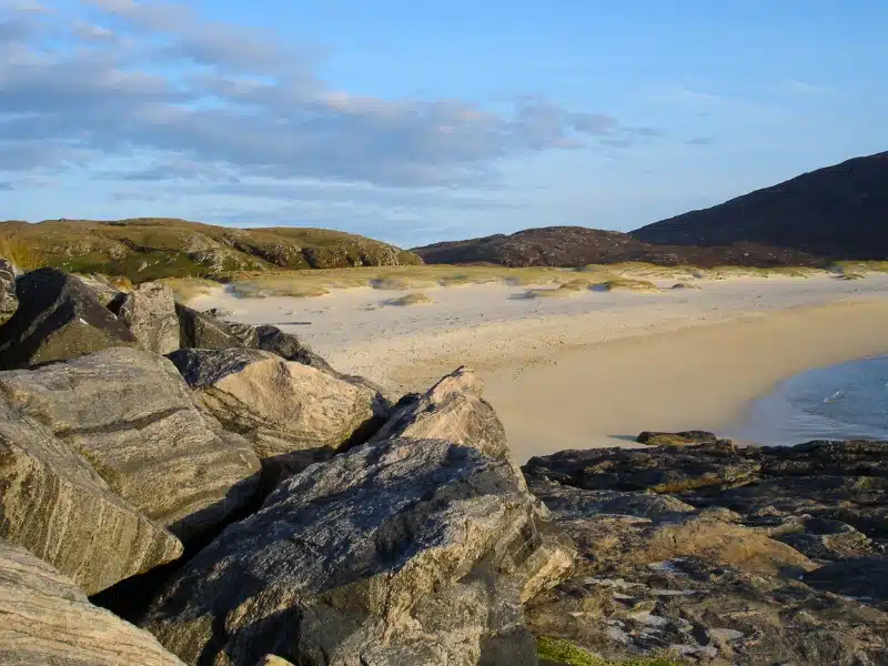 white sandy beach with a rocky foreshore and grassy dunes in the background