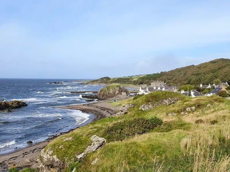 dark sandy beache backed by low grassy cliffs and small white houses