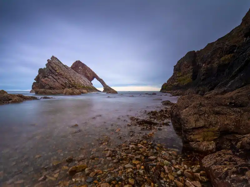 rock in the sea with an arch and hole, with smaller rocks in the foreground