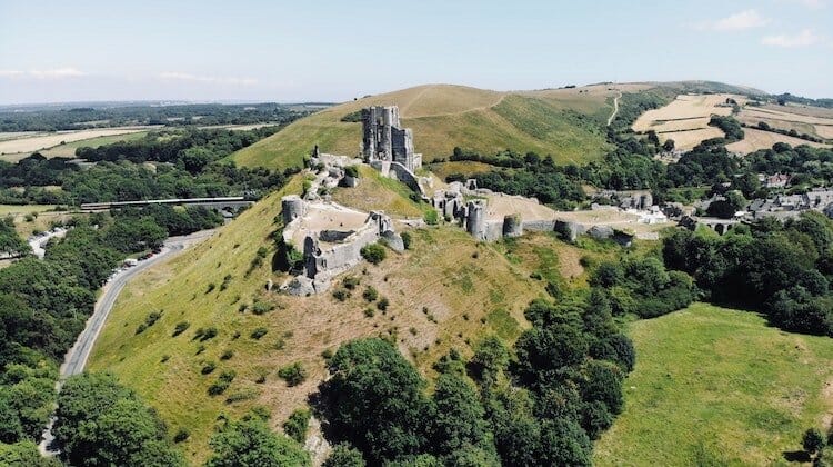 Ruined Corfe Castle amid green fields and blue skies