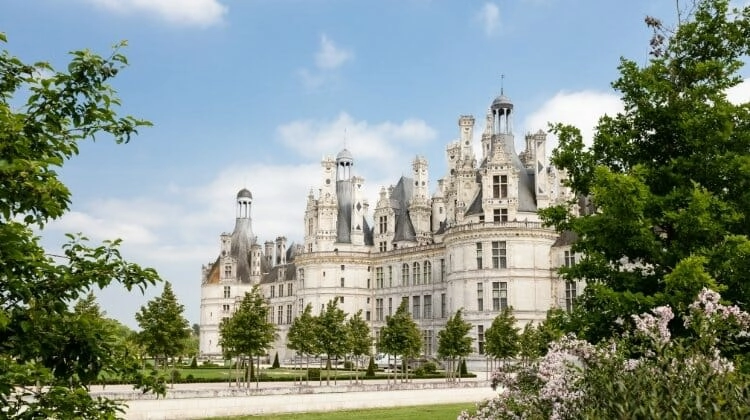 Fine French chateau with turretssurrounded by lush grass and foliage