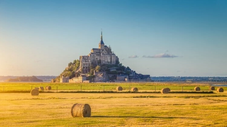 Mont Saint-Michel seen across a golden field of wheat with a blue sky