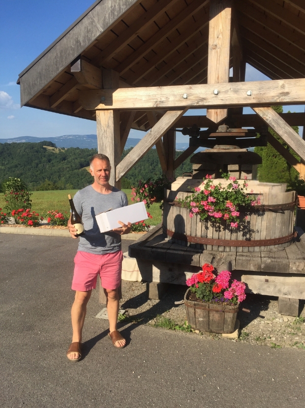 man in front of a wooden press holding a box of wine