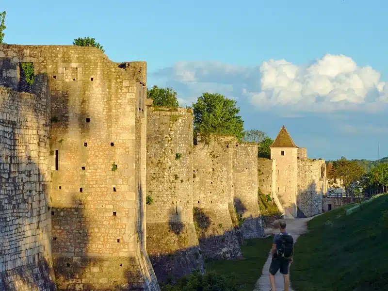 Man standing by large block stone walls with ramparts and towers in the evening sun