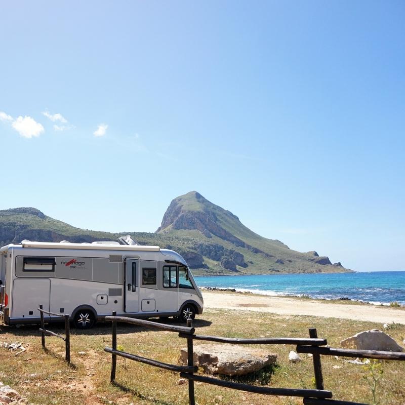 motorhome parked by a beach with turquoise sea and mountains in the background