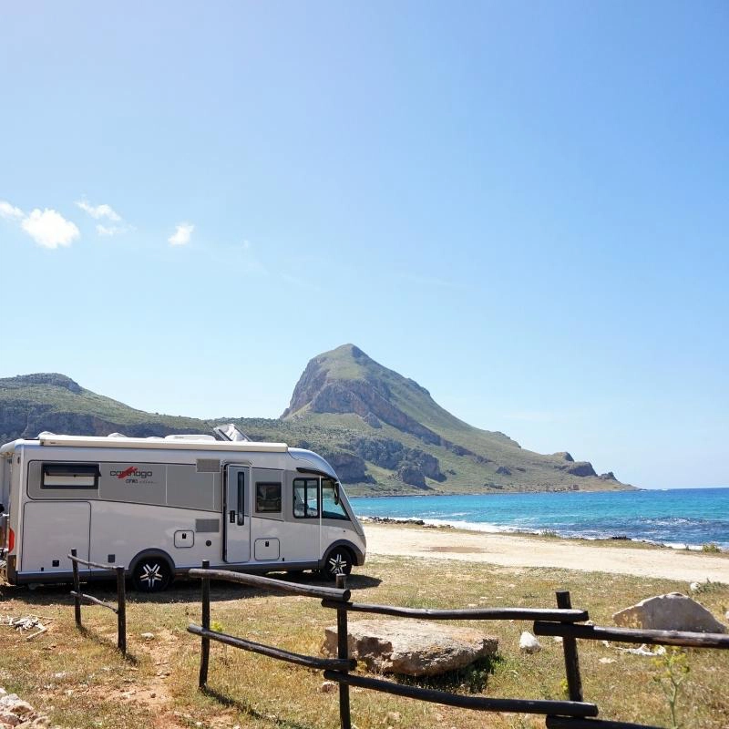 motorhome parked by a beach with turquoise sea and mountains in the background