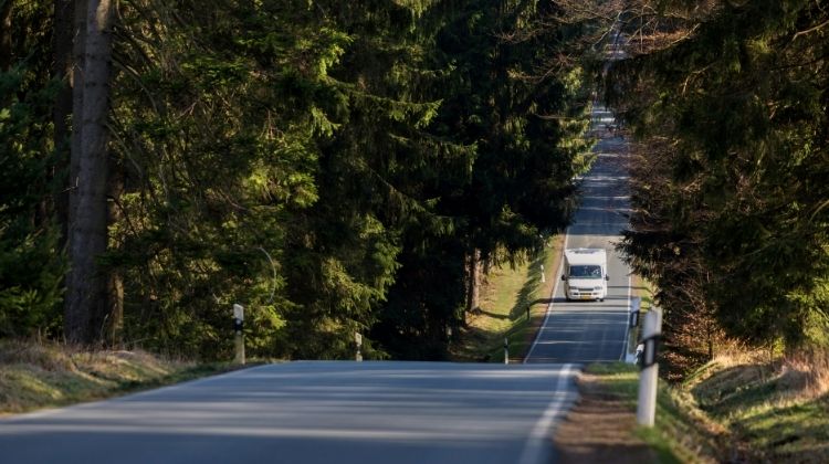 a motorhome driving along a tarmac road surrounded by trees