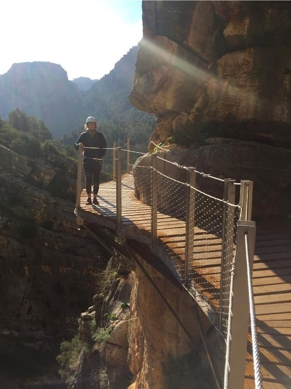 Person wearing a hard white hat on a suspended wooden boardwalk against a cliff