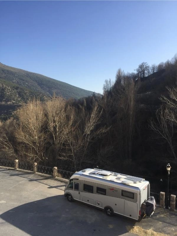 Silver motorhome parked on a bridge with mountains in the background