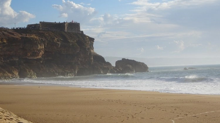 A hazy beach with frothing sea against a large cliff