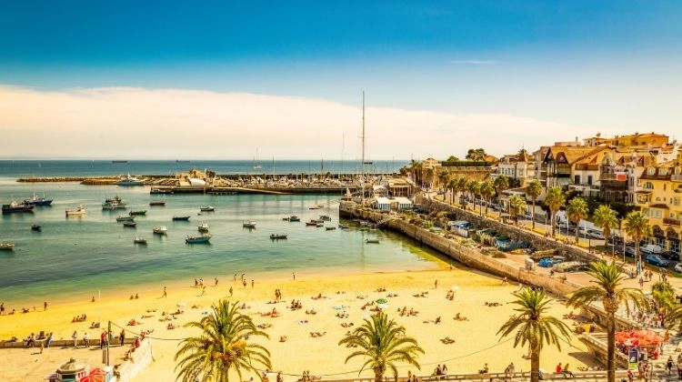 busy beach and yacht filled cove with buildings and a promenade