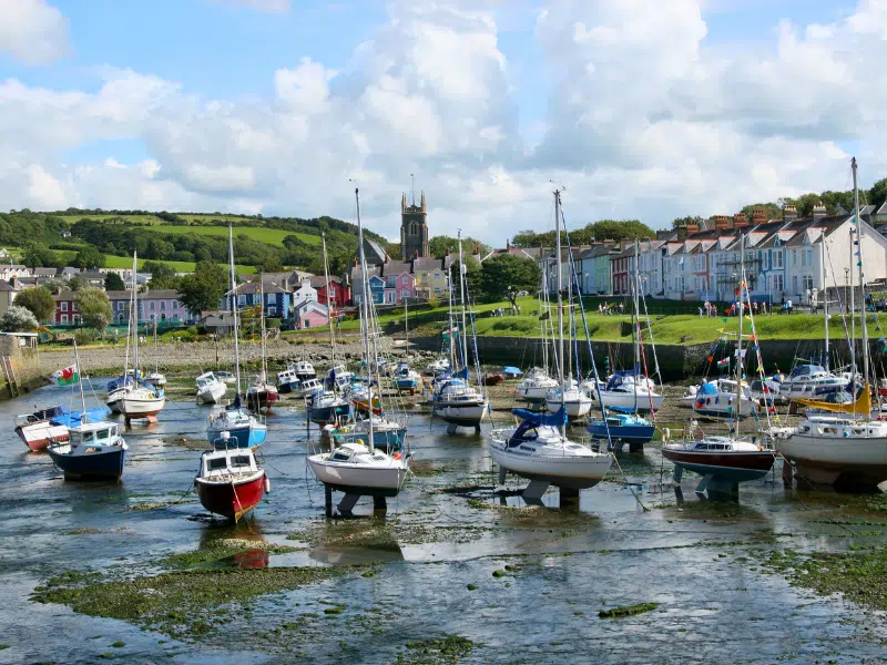sailing boats in a small harbour with the tide out, with colourful houses as a backdrop