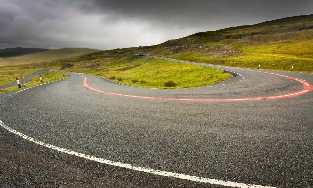 Tight bend on a tarmac road through a grassy mountainous landscape