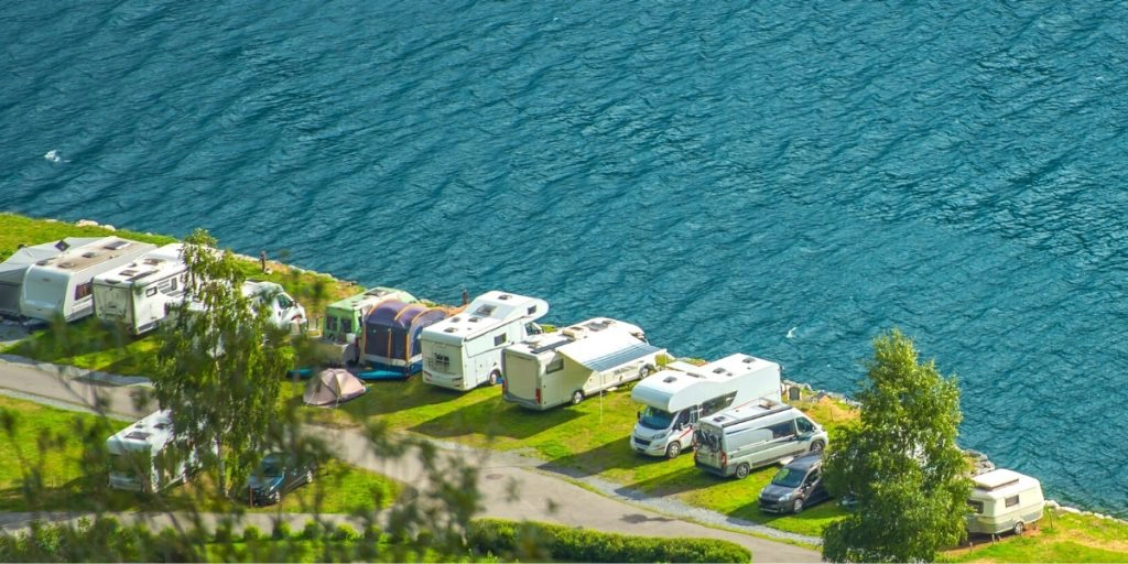 motorhomes and campervans parked on grass by a turquoise lake