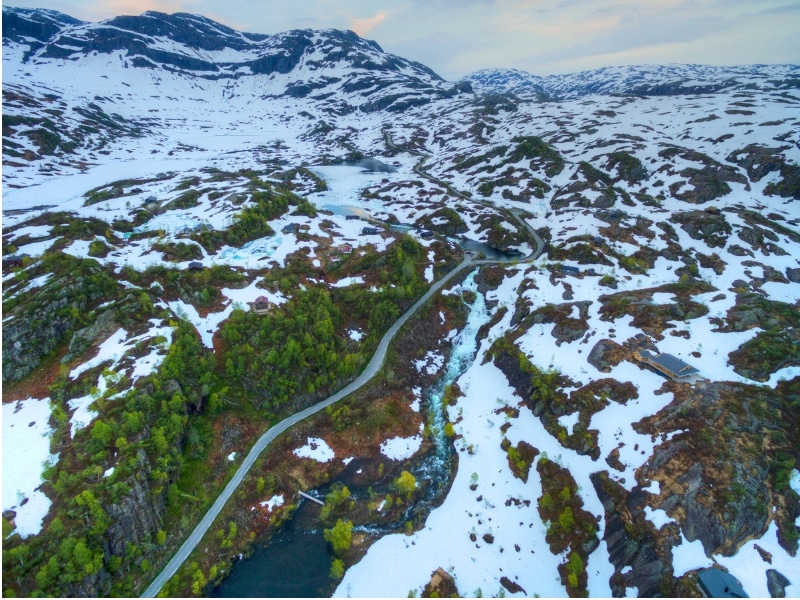 road though snowy fields with trees past a waterfall and river