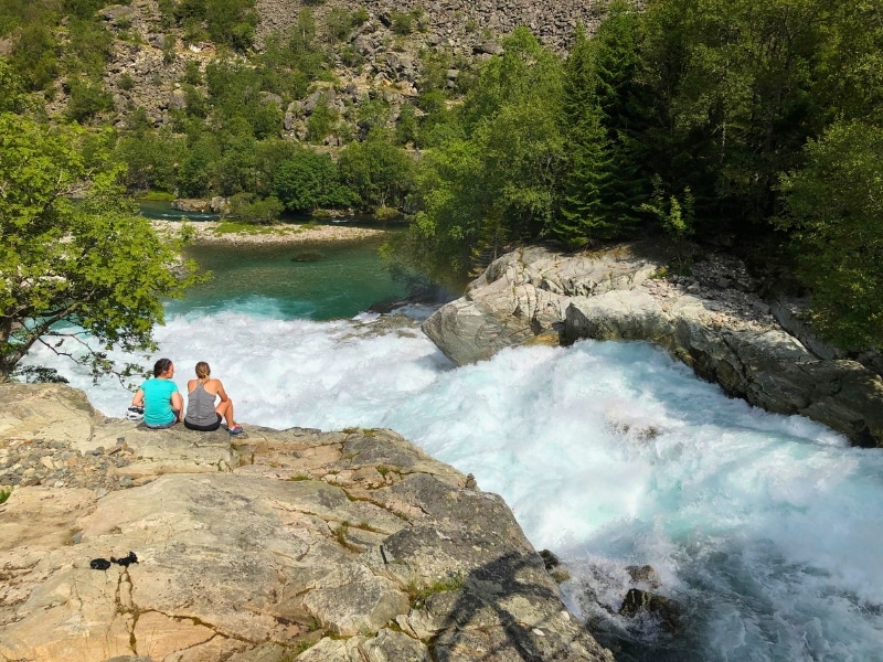 two women sitting on a rock overlooking a waterfall