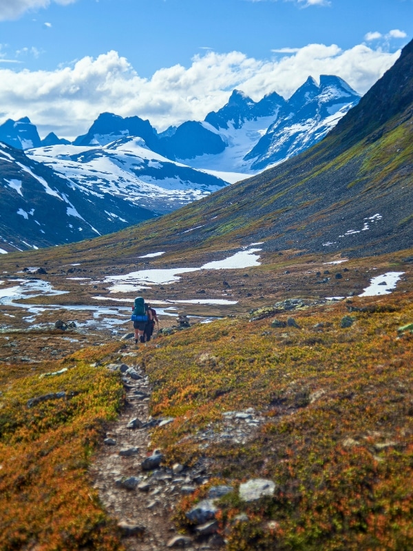 people hiking on a narrow path towards a deep valley with towering mountains