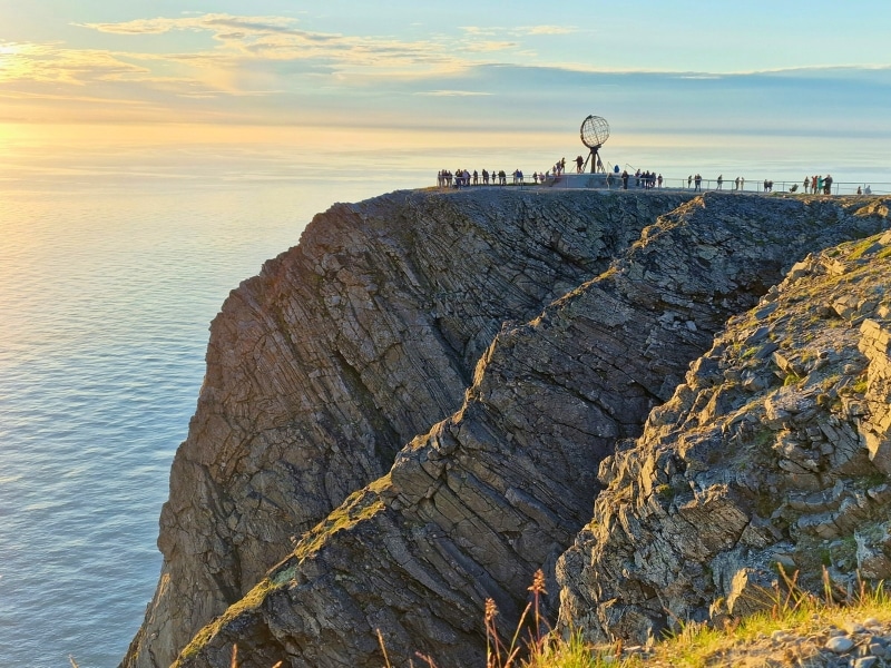 people standing on a high rocky cliff around a globe monument