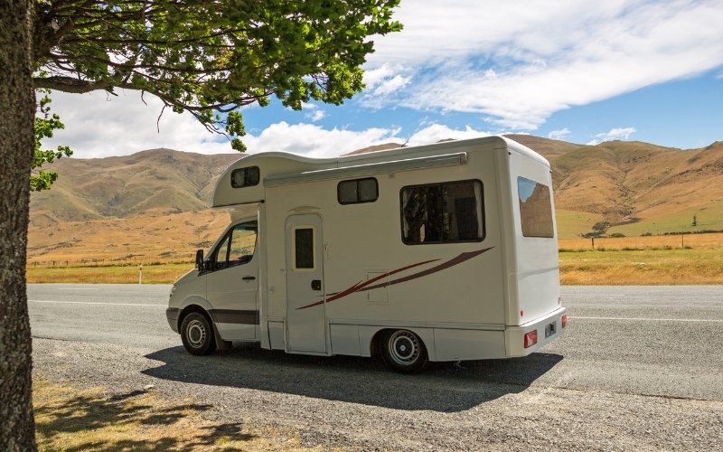 motorhome in a road in front of rollong hills with a tree in the foreground