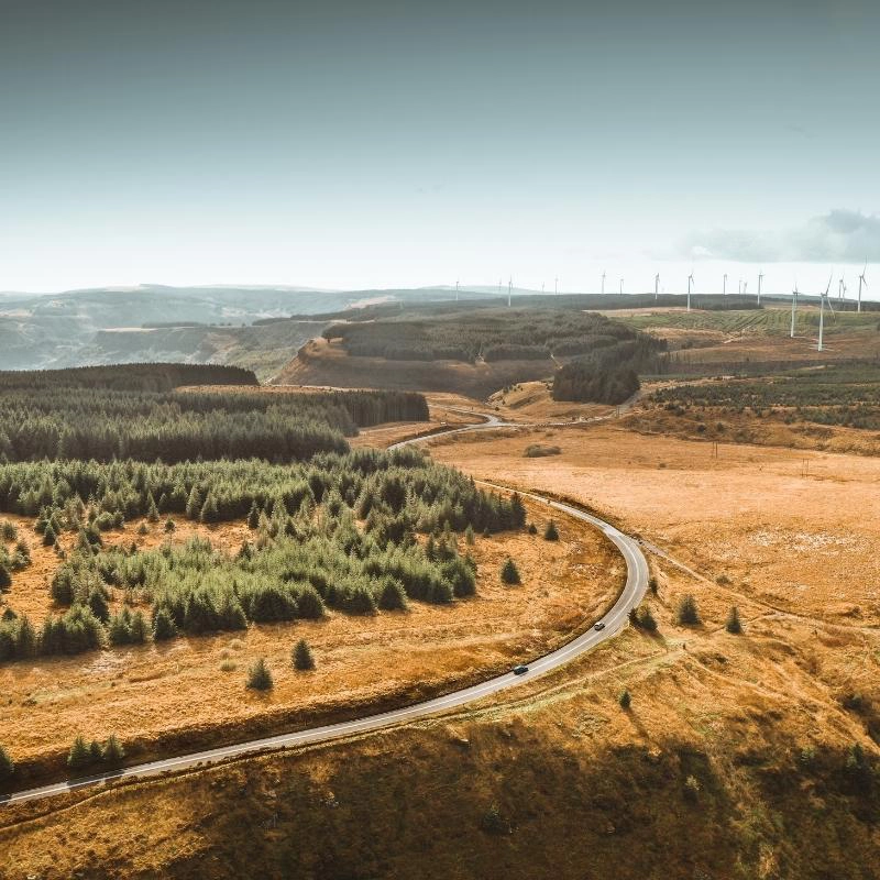 narrow road with two vehicles driving on it snaking through the brown and green Brecon Beacons mountains in Wales