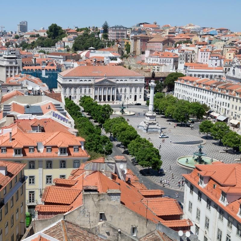 Elegant paved square with a central statue surrounded by large white buildings with teraccotta tiled roofs