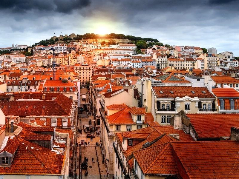 a view across terracotta rooftops to a hill and a castle in the distance