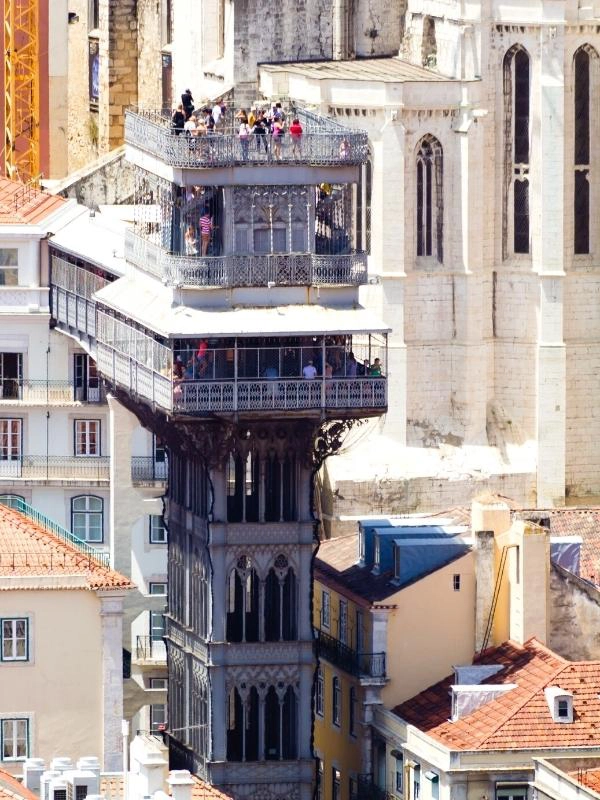 Tall wrought iron structure housing an elevator, surrounded by creamy stone buildings