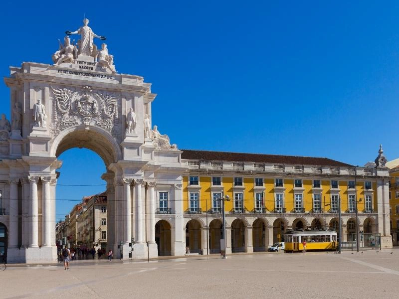 large ornate white stone arch next to yellow building with many upper floor windows and ground floor arches