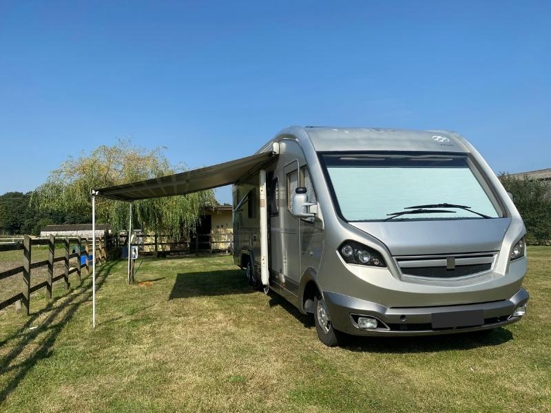 large silver motorhome parked in a grassy field with awning out