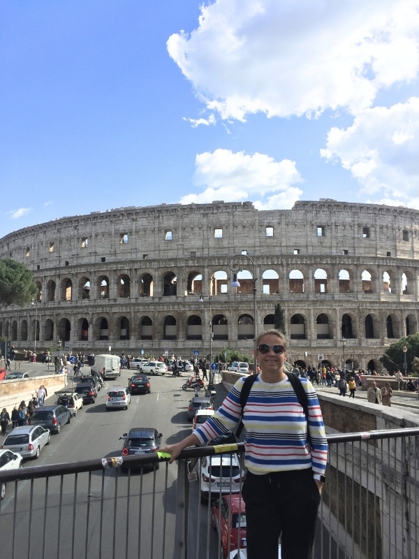 woman in a stripy jumper standing on a bridge in from of Rome's Colosseum